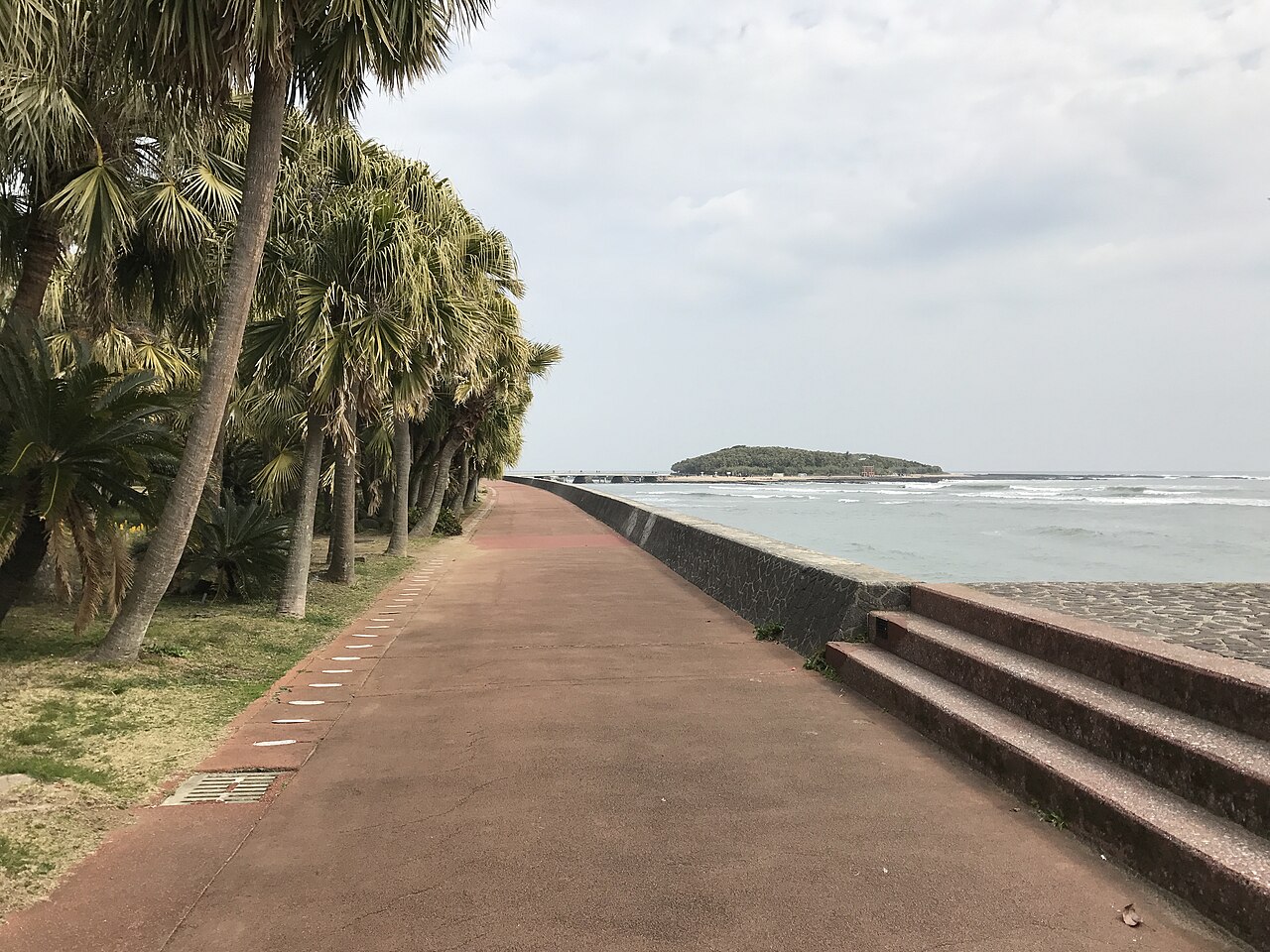 Palm-lined seaside promenade with the island of Aoshima on the horizon