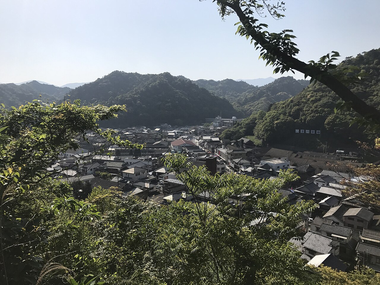 Arita town packed into a narrow valley between forested hills, seen through trees from the hill near the Ri Sampei monument