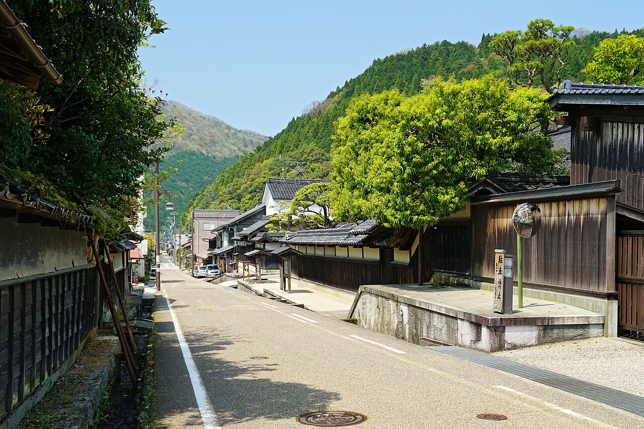 Quiet street of tile-roofed wooden merchant houses and long walls in the Chizu post town, with wooded hills behind