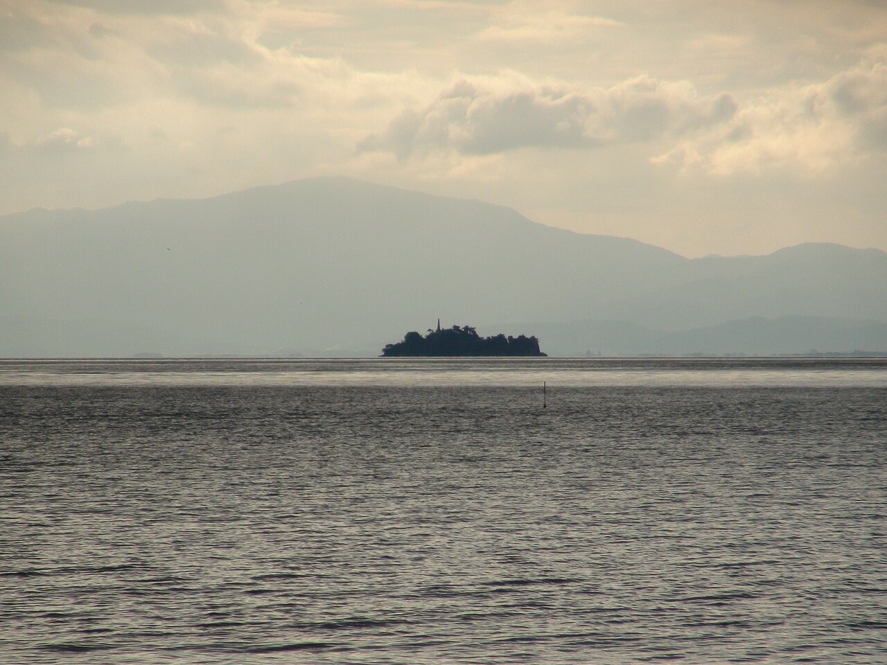 Take Island seen across the calm water of Lake Biwa from the Matsubara shoreline near Hikone, with hazy hills along the far side of the lake.