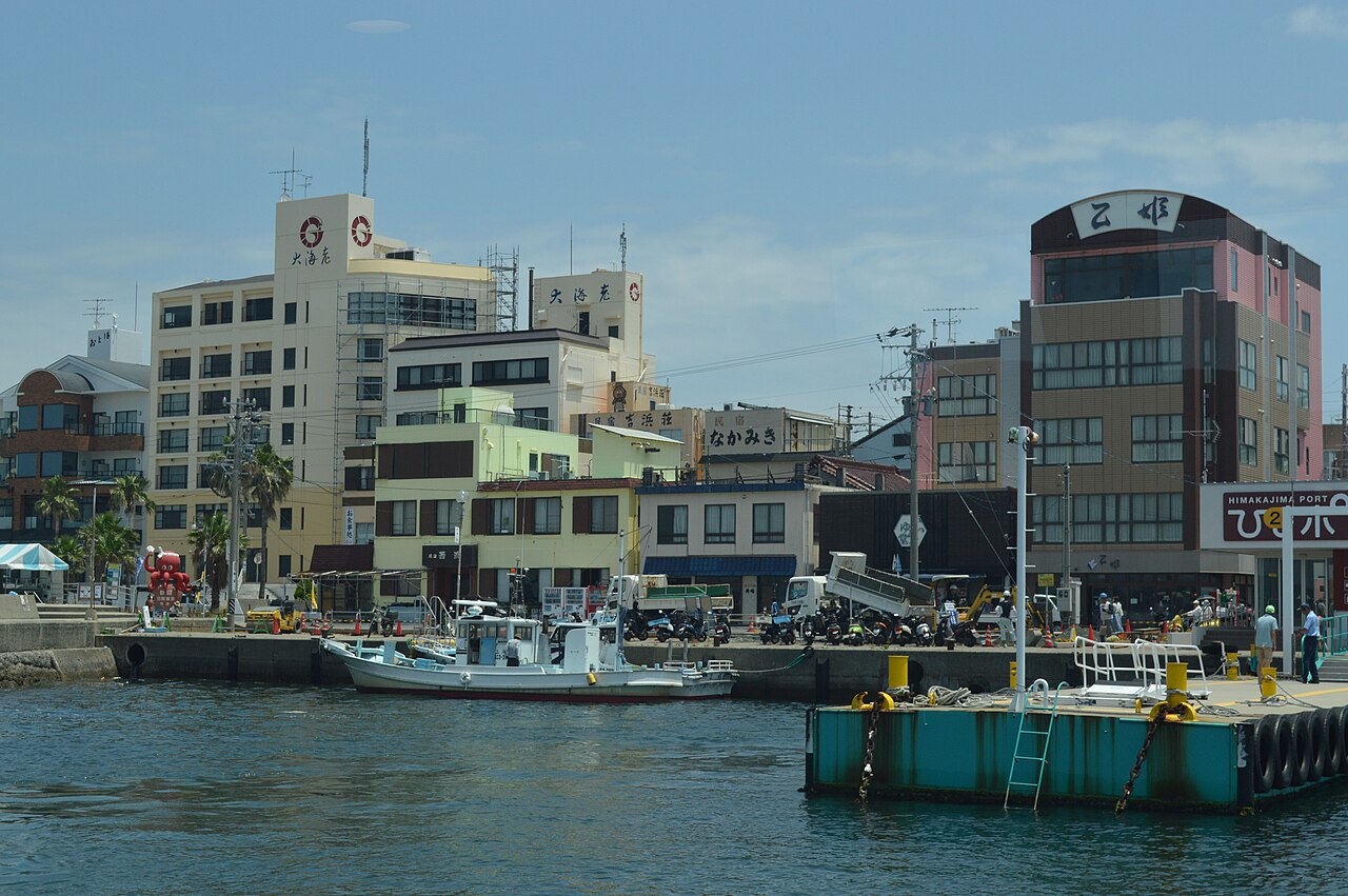Inns and guesthouses lining the harbor at Himakajima West Port, with fishing boats moored along the quay.