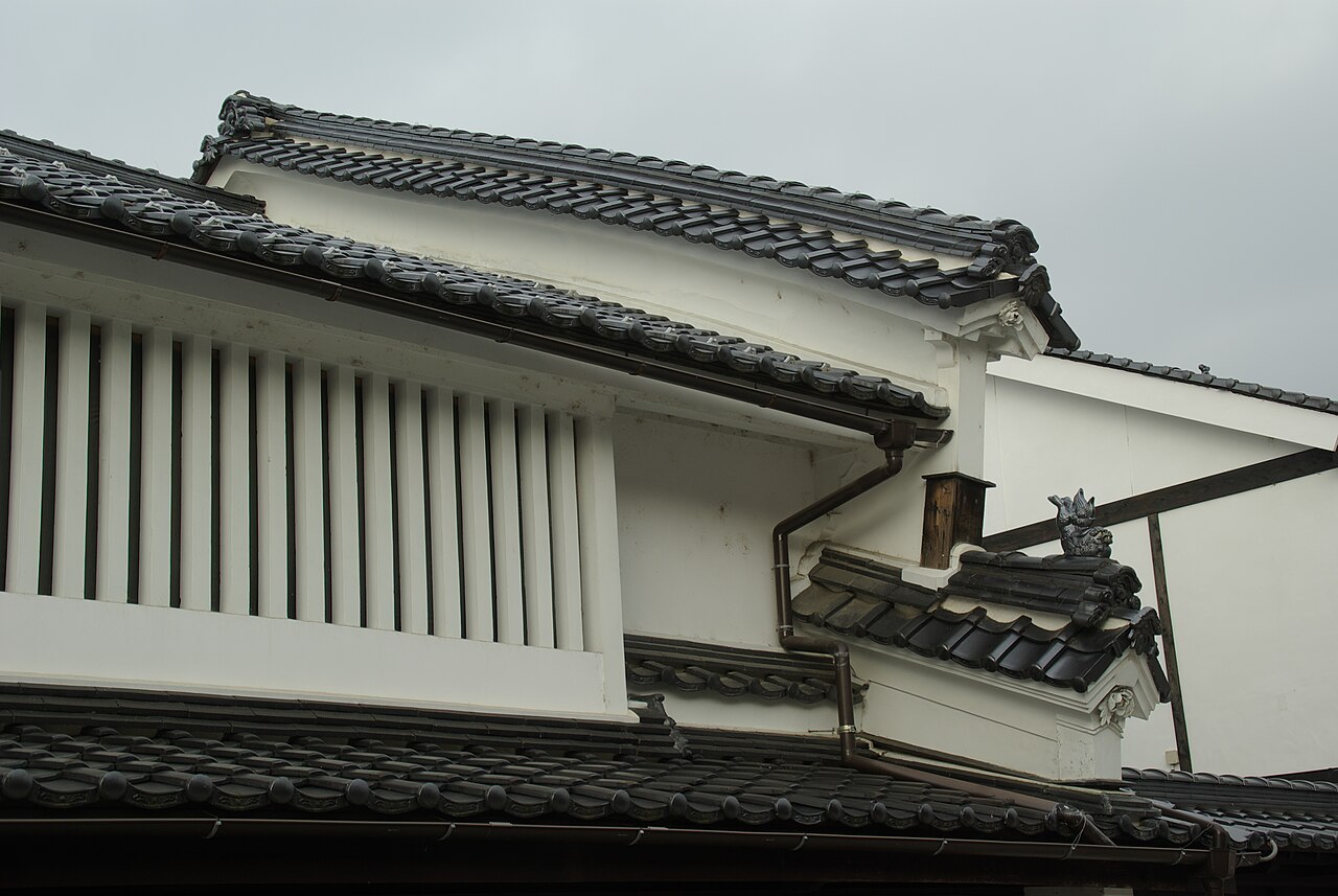 The white plastered wall of an old merchant house with vertical lattice windows, layered dark tile eaves and a small ridge ornament.