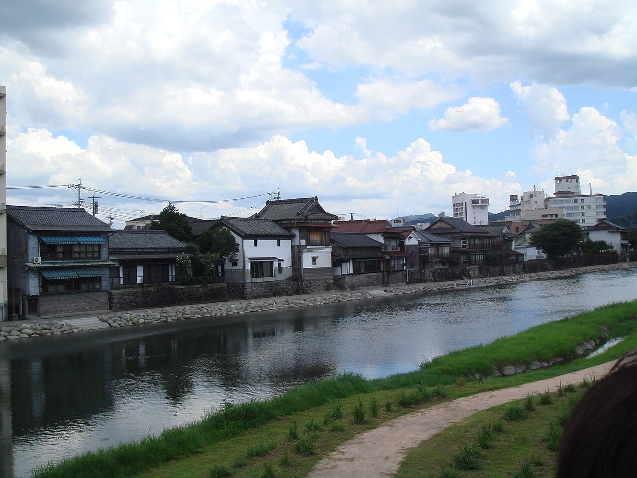 Old wooden houses lining a calm river with a grassy bank and walking path in Hita, Oita