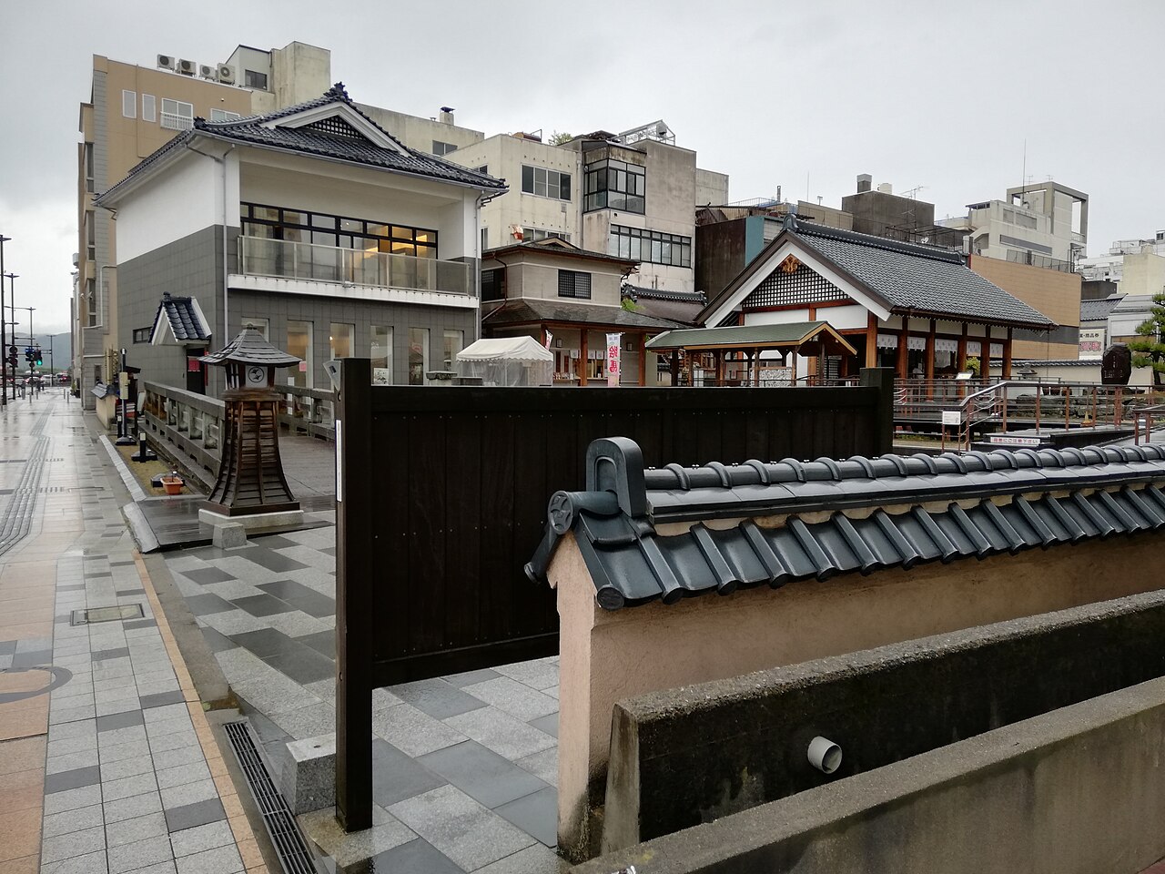 Tiled walls, a stone lantern and a wooden bridge beside the Shibata Shrine in central Fukui, on a rainy day.