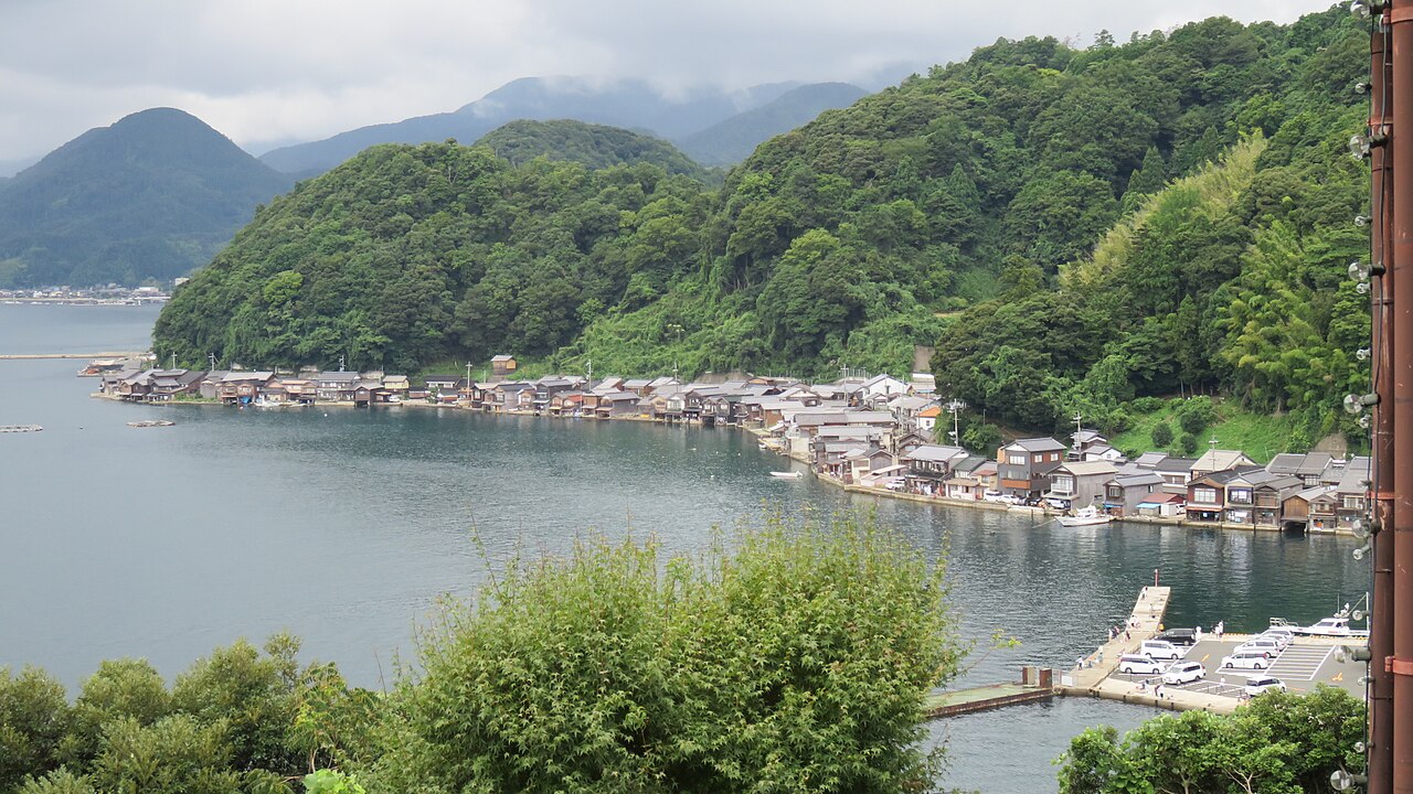 View from a hillside overlook down onto a row of funaya boathouses lining the bay.