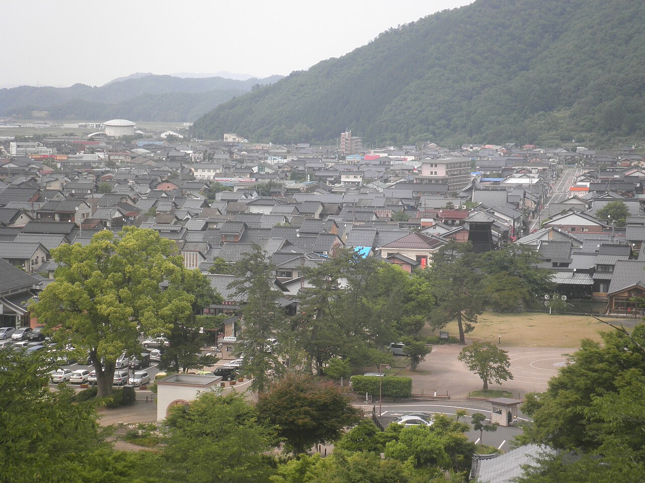 A view over the roofs of Izushi's castle town from the castle hill, with the clock tower among the houses and green mountains behind.