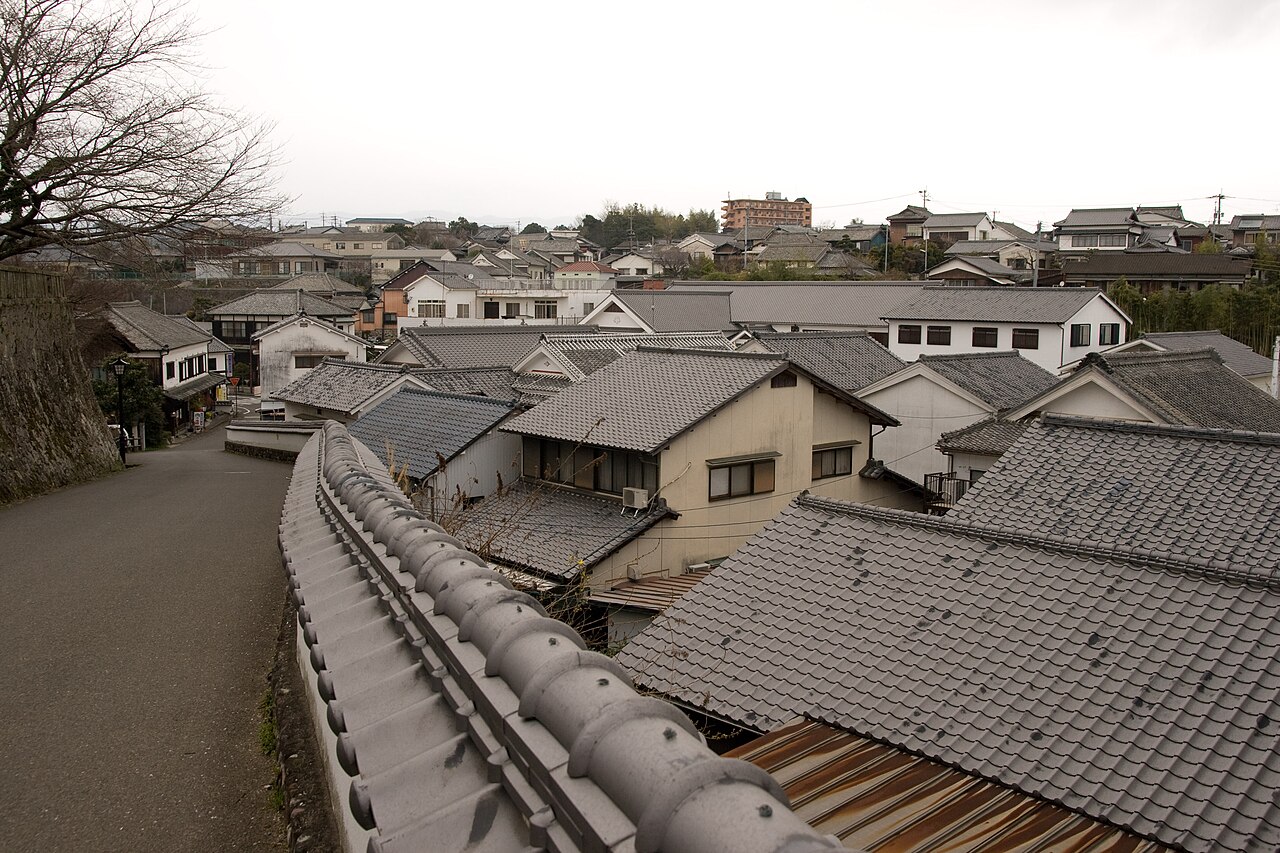 Tiled rooftops and a low earthen wall in Kitsuki's old castle town, seen from a slope above the lanes