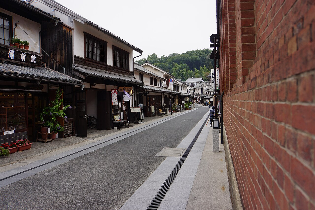 A quiet paved street lined with old two-story wooden townhouses with latticed fronts and a red brick wall on the right.