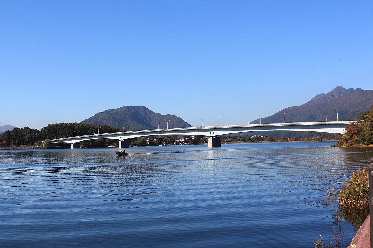 Kawaguchiko Ohashi bridge spanning the lake under a clear blue sky, with wooded mountains beyond.