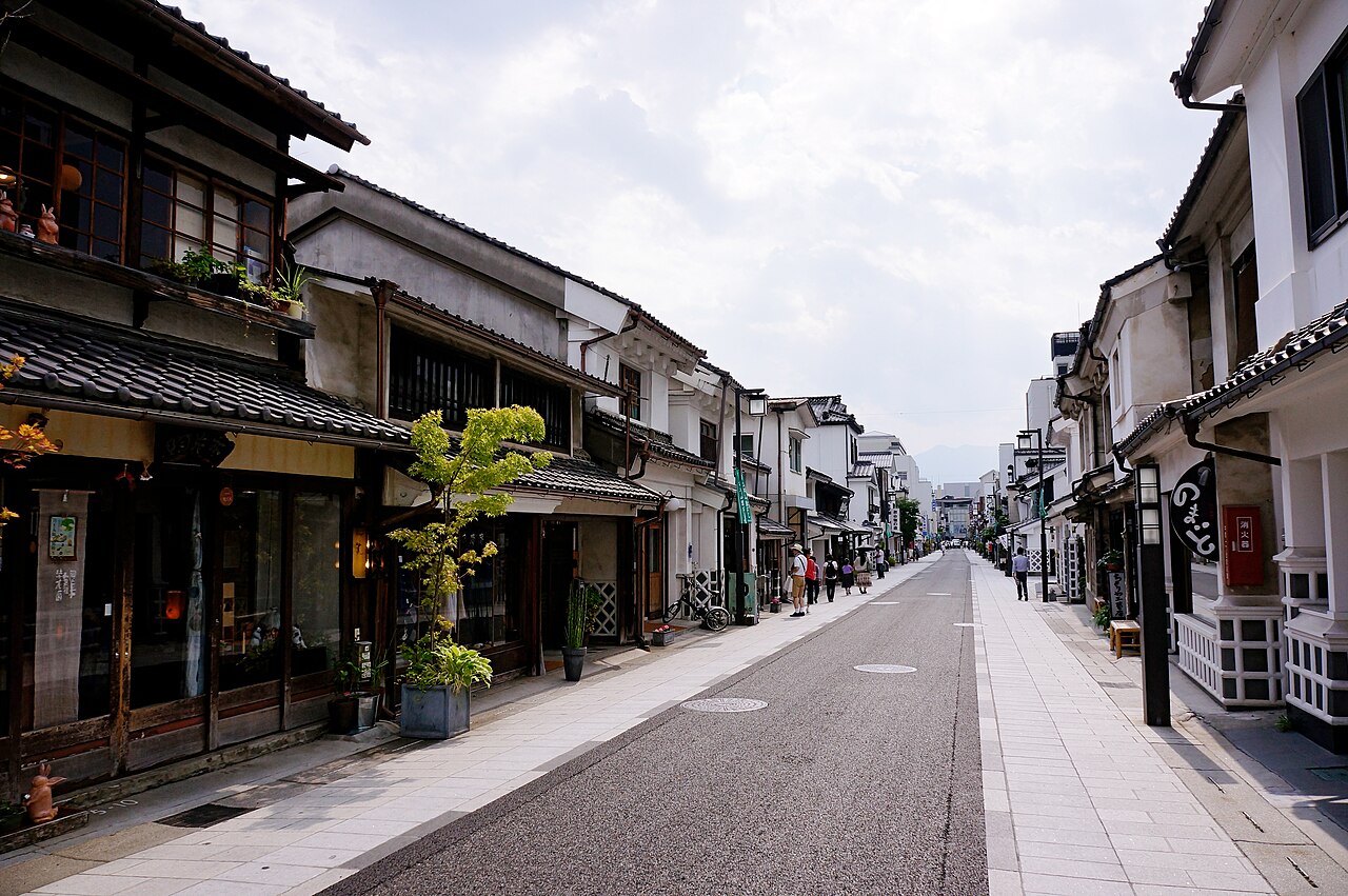 Quiet Nakamachi street in Matsumoto lined with white-walled kura storehouse shops and old wooden townhouses, with a few strollers in the distance.