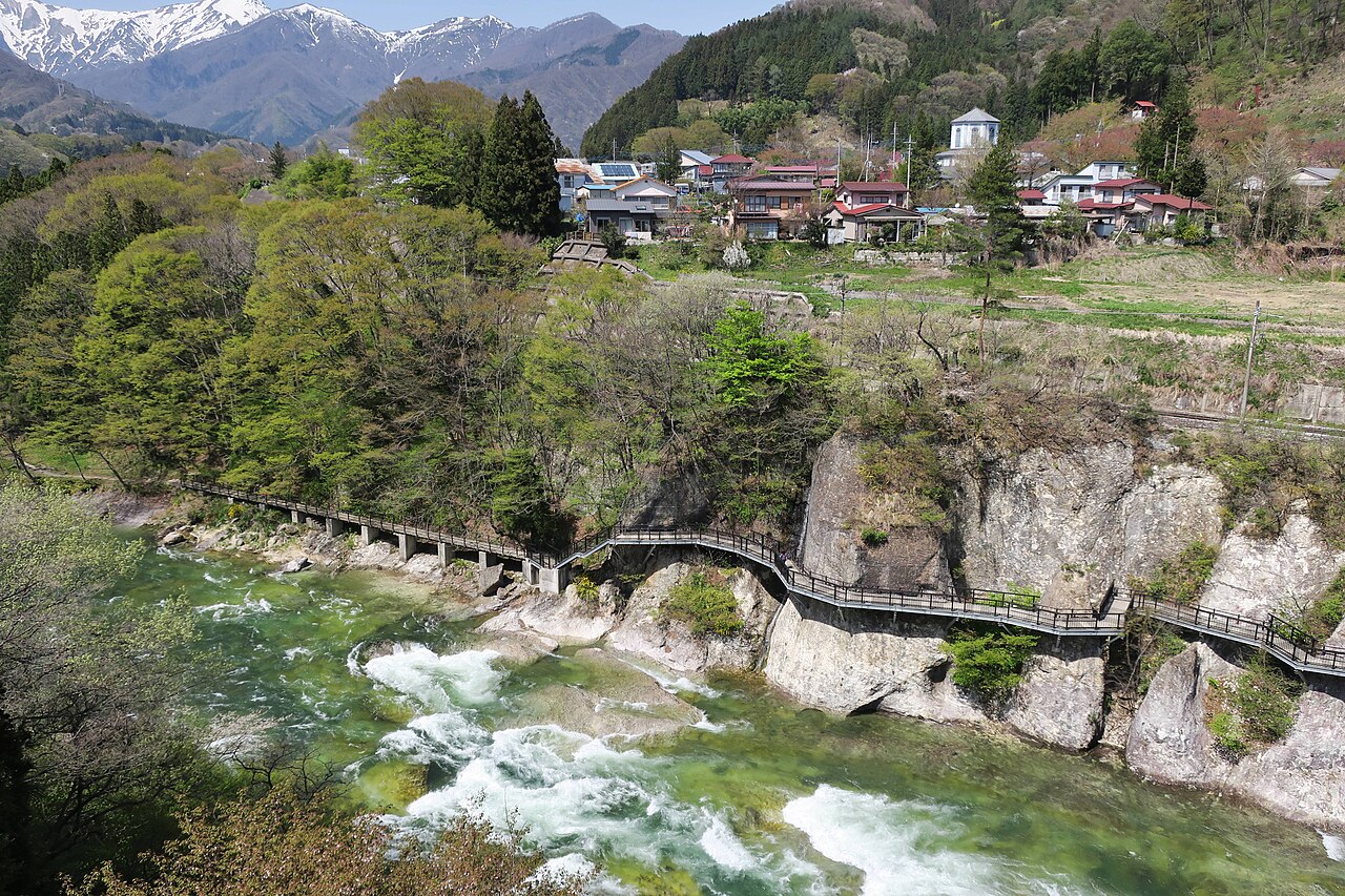 Riverside town buildings of Minakami and a gorge promenade, with snow-capped mountains behind