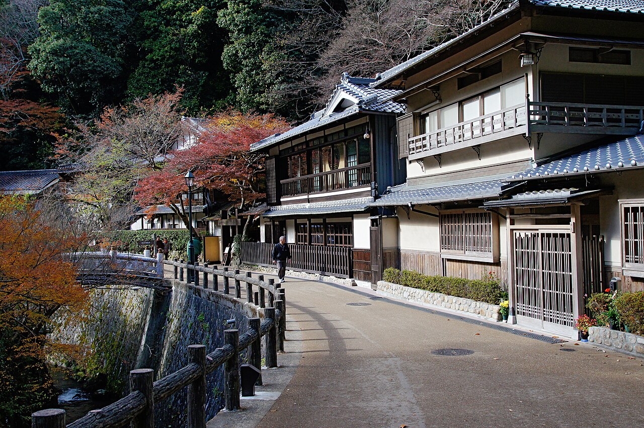 A quiet street of traditional buildings along a mountain stream in Minoh, with autumn maple color overhead.