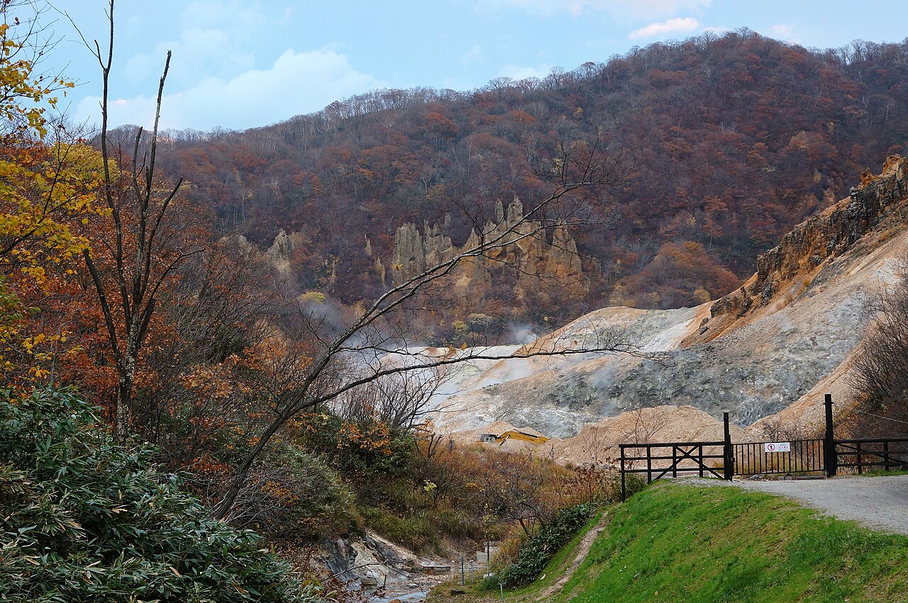 Autumn colour on the ridges above Noboribetsu, with pale steaming ground and a gravel track leading down into the valley.