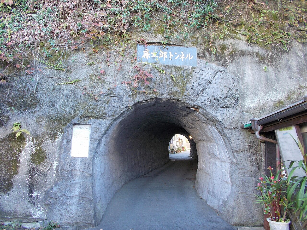 Stone tunnel entrance with a signboard reading Rentaro Tunnel on a hillside in Taketa, with a narrow lane and houses visible at the far end