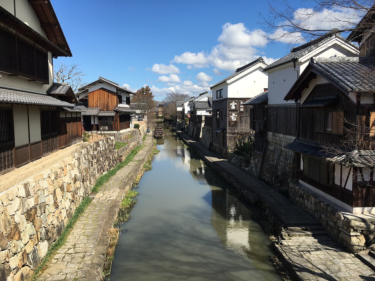 A stone-walled canal lined with old white-walled merchant houses in Omihachiman under a blue sky.