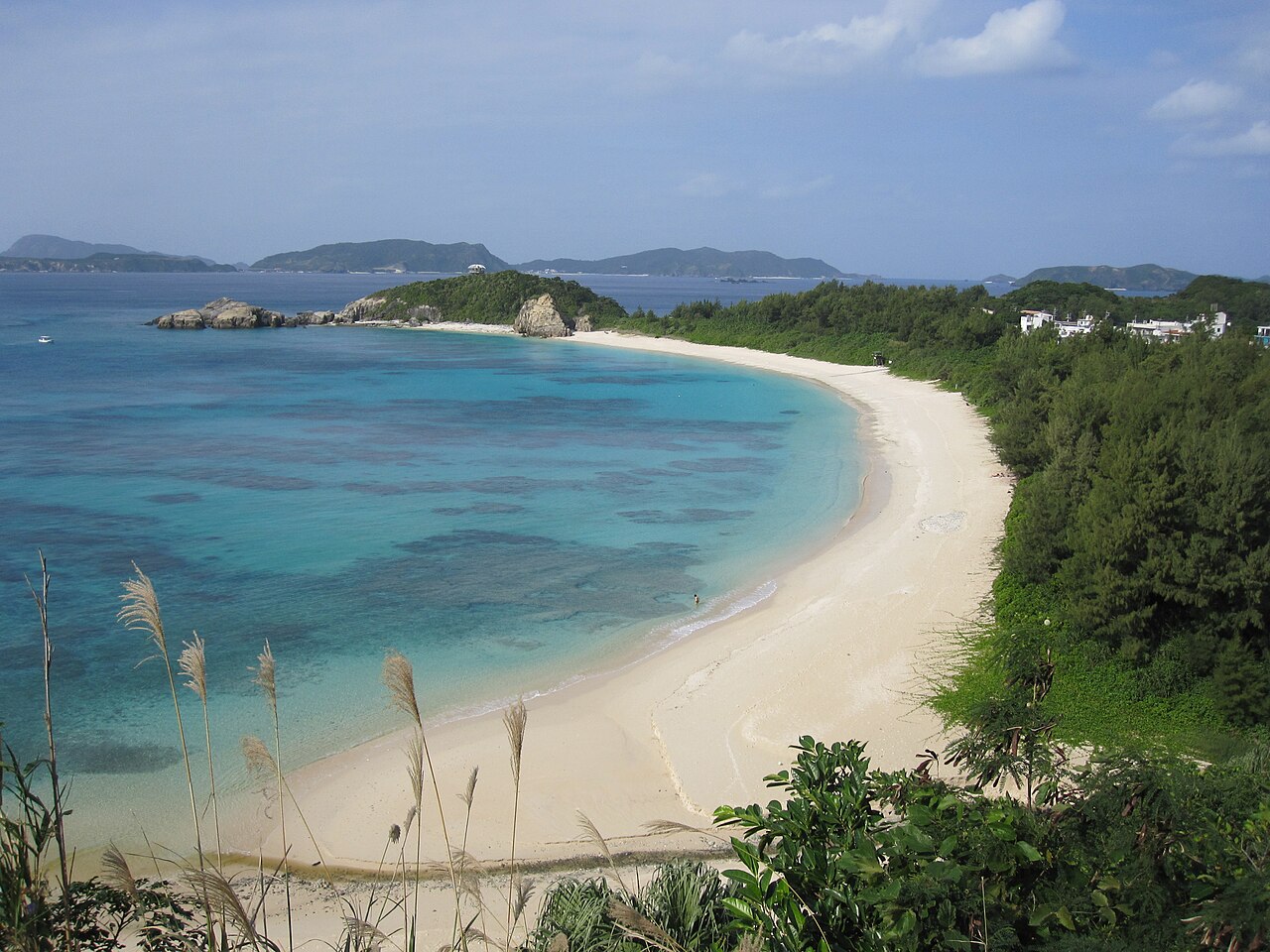 The long white crescent of Aharen Beach on Tokashiki Island seen from a hillside, with turquoise water and low green hills