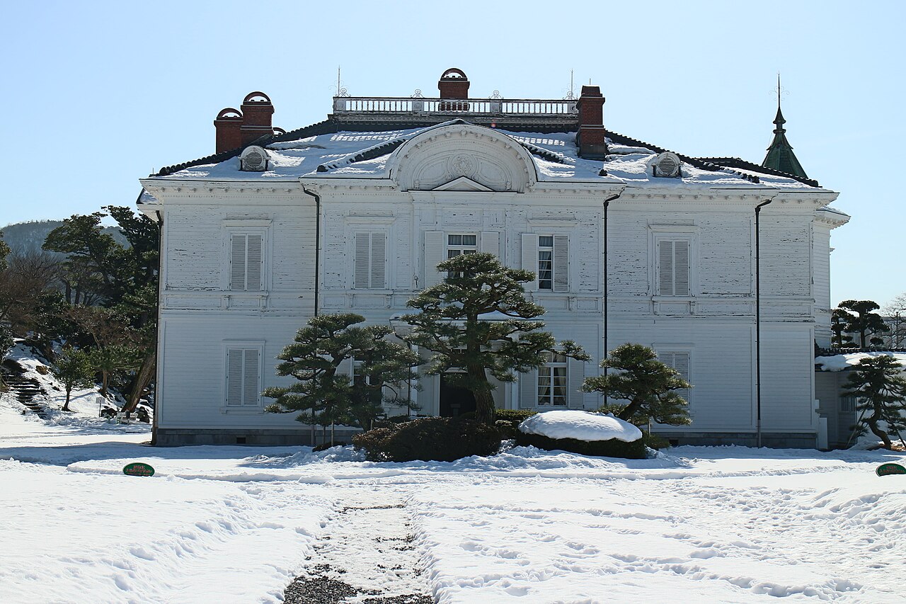 the white Western-style Jinpukaku mansion in Tottori Castle Ruins Park, its roof dusted with snow beside trimmed pine trees