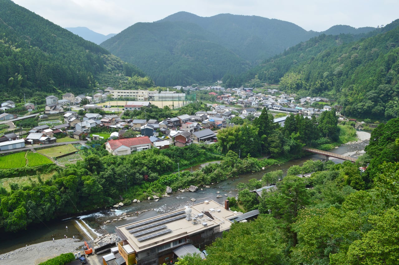 An overview of the small village of Umaji, its houses scattered along a river valley surrounded by forested mountains in Kochi Prefecture.