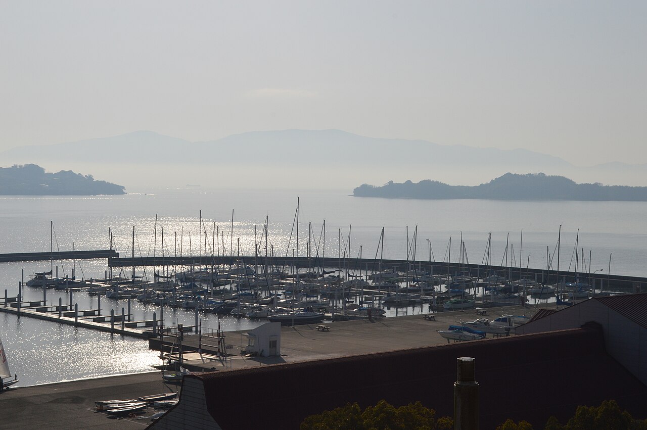 Ushimado Yacht Harbor in soft haze, rows of sailboat masts inside the breakwater with Seto Inland Sea islands beyond