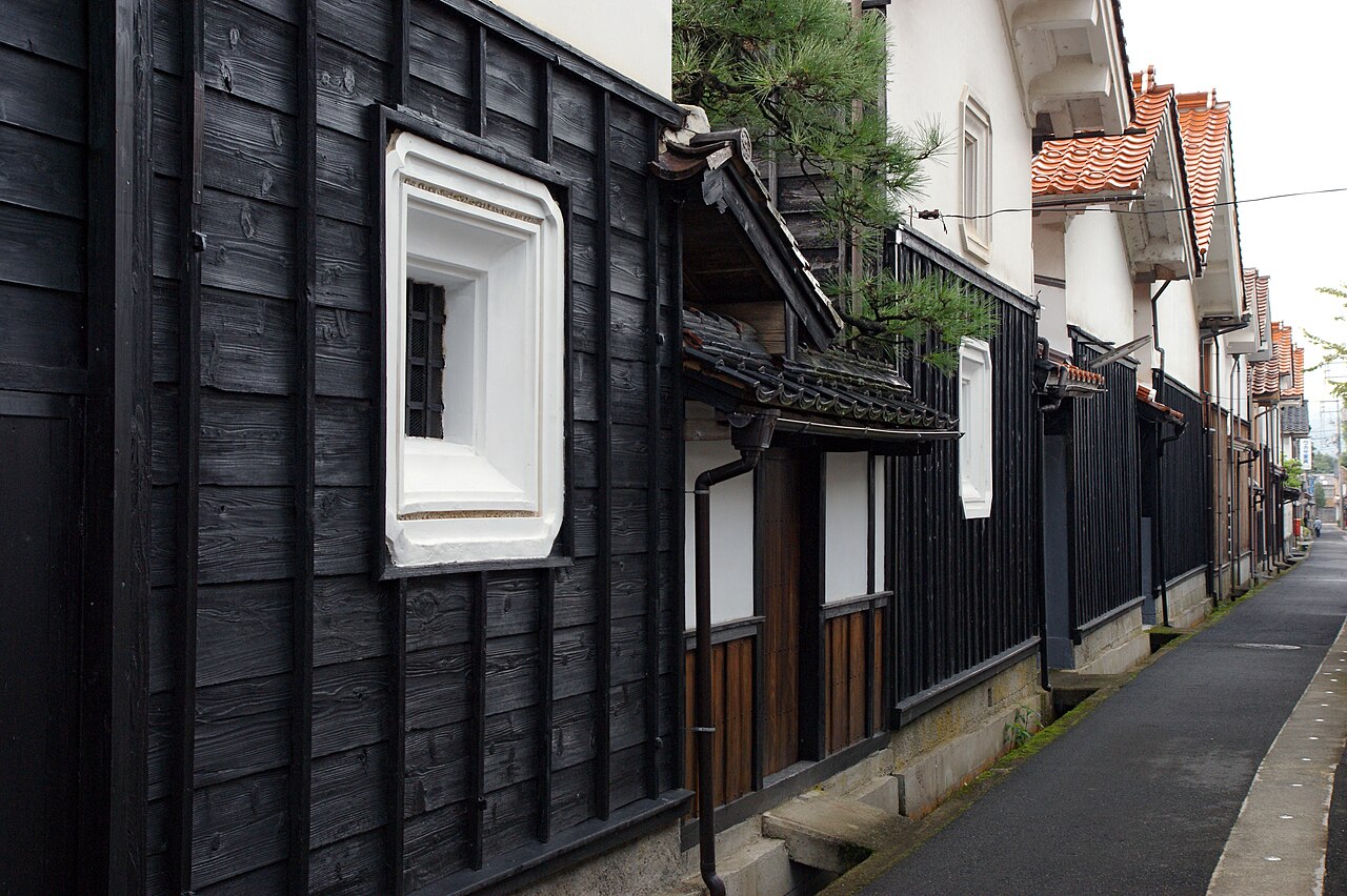 A quiet paved lane in Wakasa lined with black timber storehouses, white plaster walls and orange tile roofs
