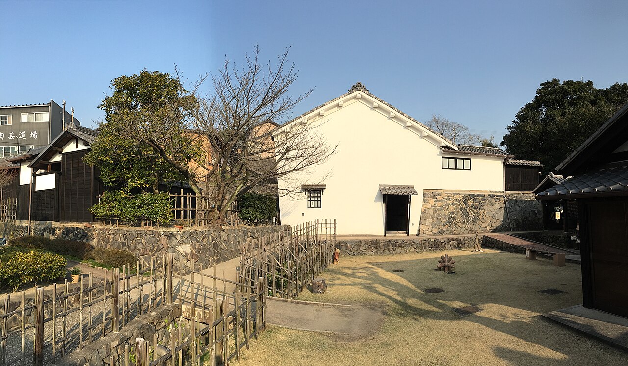 The white-walled storehouse and garden of the Takita family's old shipping-merchant house in Tokoname, with a brick kiln chimney behind it