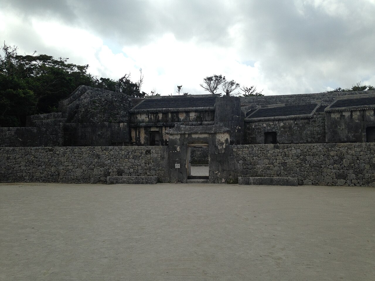 A low stone gate set into the coral-limestone perimeter wall of Tamaudun, the royal mausoleum of the Ryukyu kings, with tiled-roof burial chambers visible behind the wall.