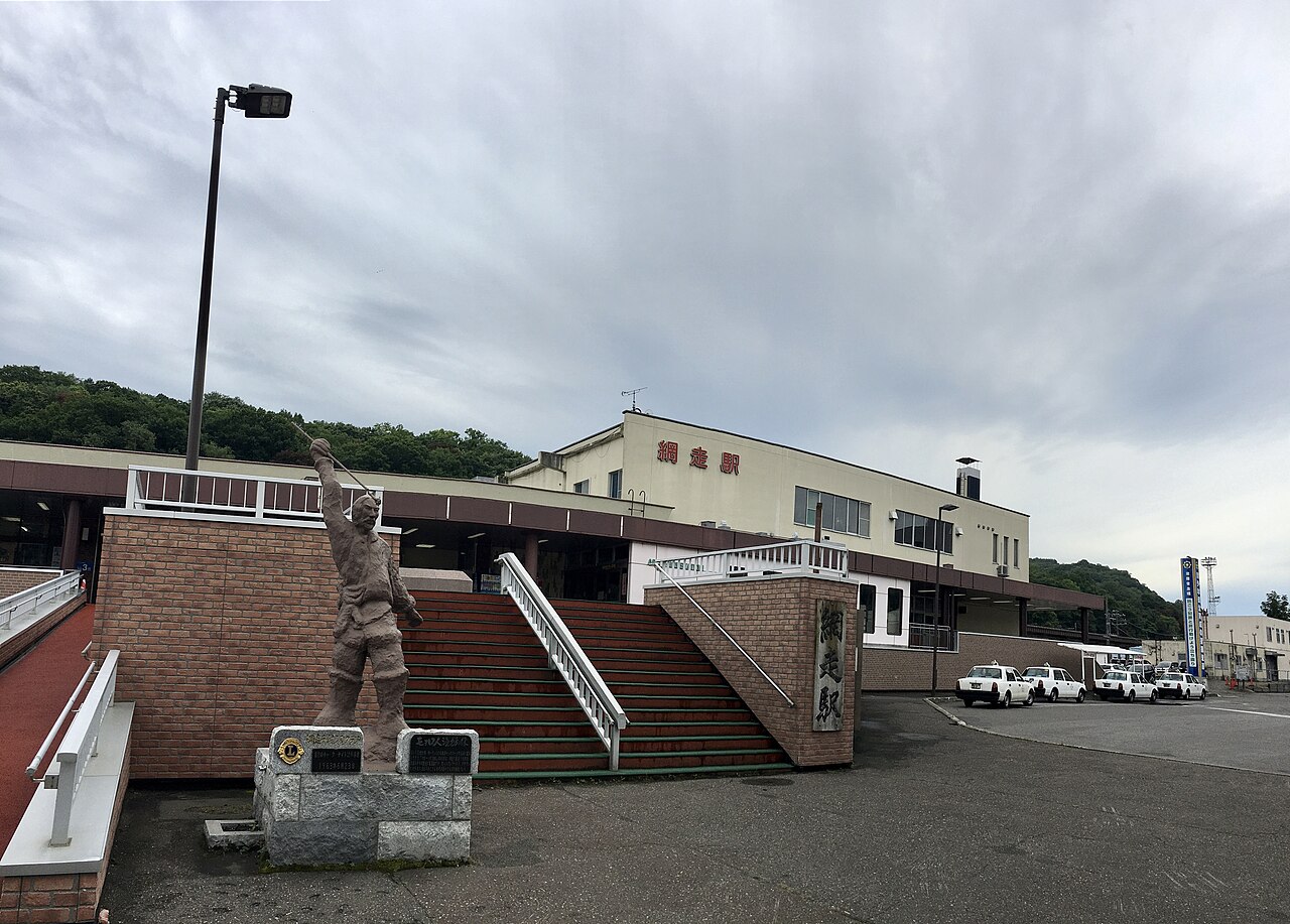 Station building and a bronze figure beside the stairs under an overcast sky