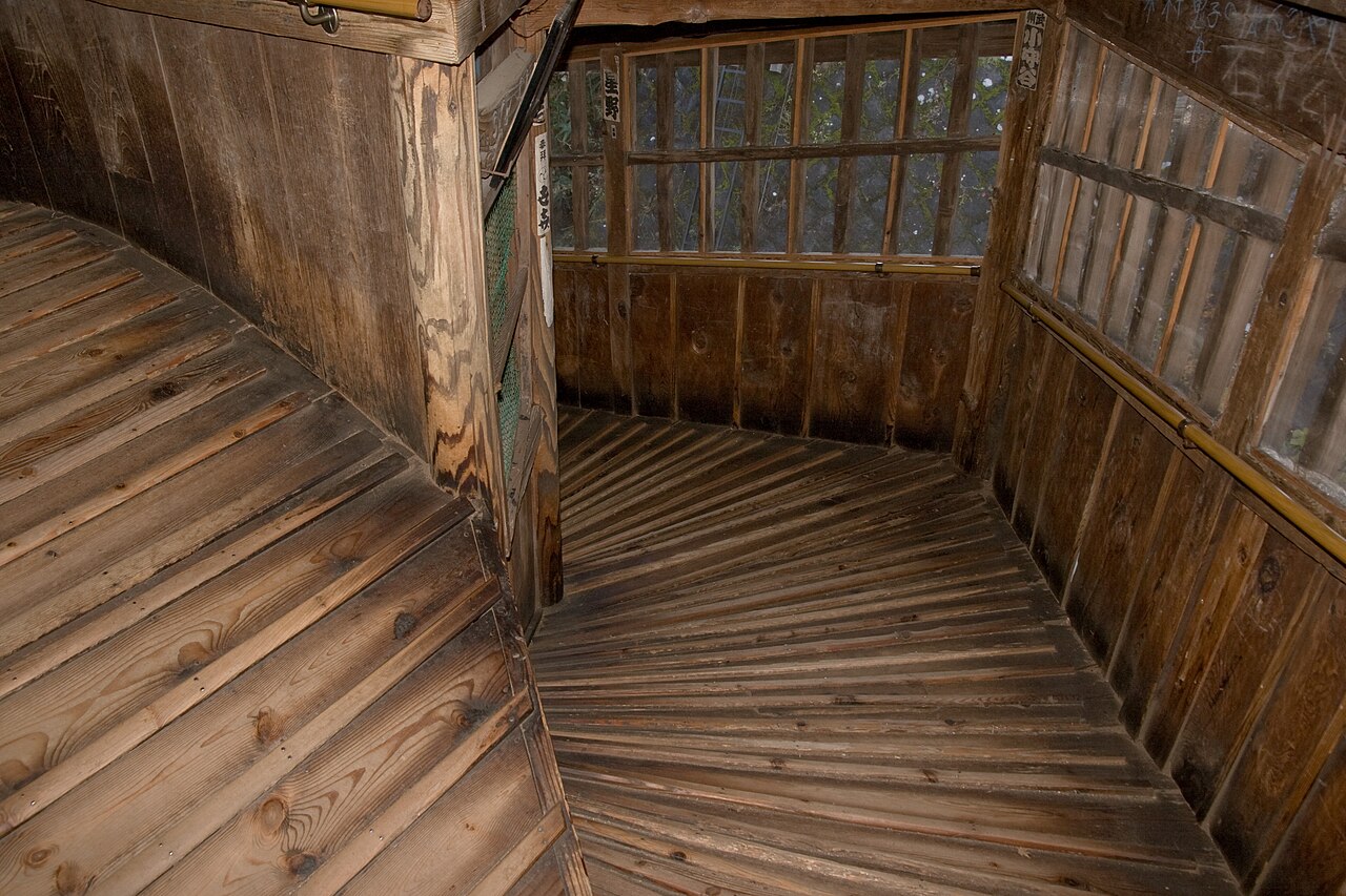 The bare cedar boards of the double-helix ramp inside Sazaedo, curving away from the viewer without a single stair tread