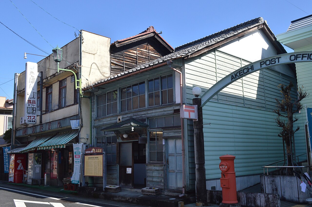 The old wooden Akechi Post Office, painted pale green, with an arched Akechi Post Office sign and a red postbox in front