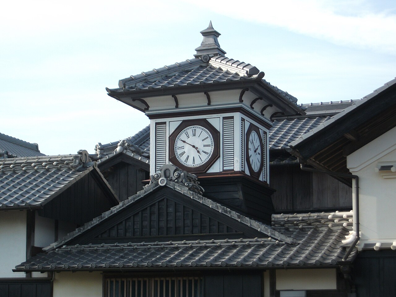 The white clock tower of the Noradokei in Aki, with an octagonal clock face and Roman numerals, rising above dark tiled roofs under a pale sky