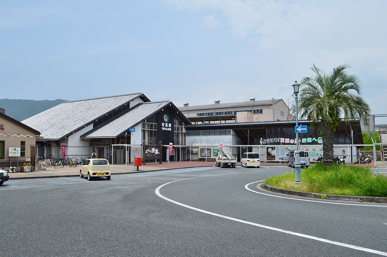 The low station building of Aki Station on the Gomen-Nahari Line, with tiled roofs, parked bicycles and a palm tree on the roundabout in front