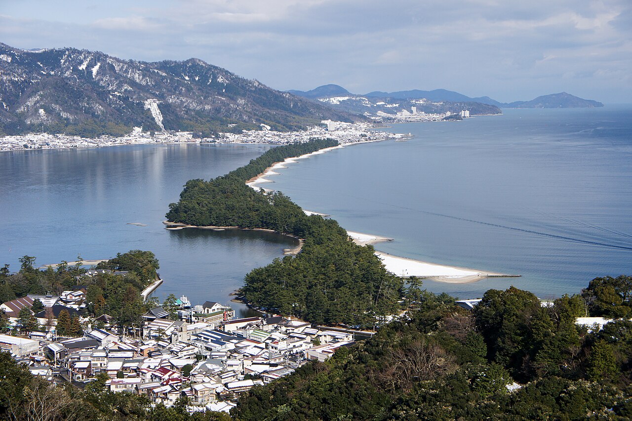 The long pine-covered Amanohashidate sandbar and snow-dusted mountains seen across the bay from the hilltop on the Monju side