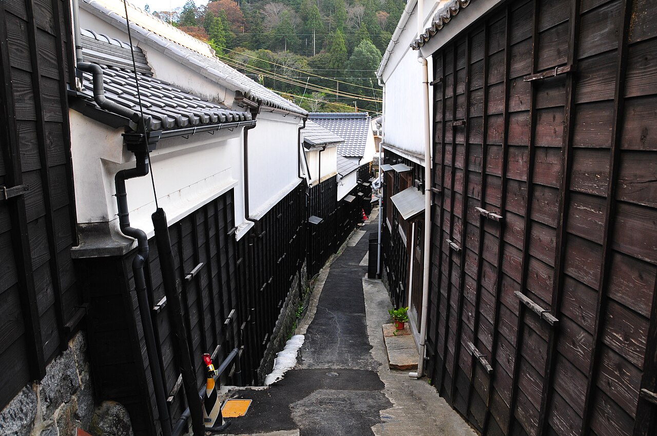 A narrow paved lane lined with black plank walls and white-walled storehouses in Asuke