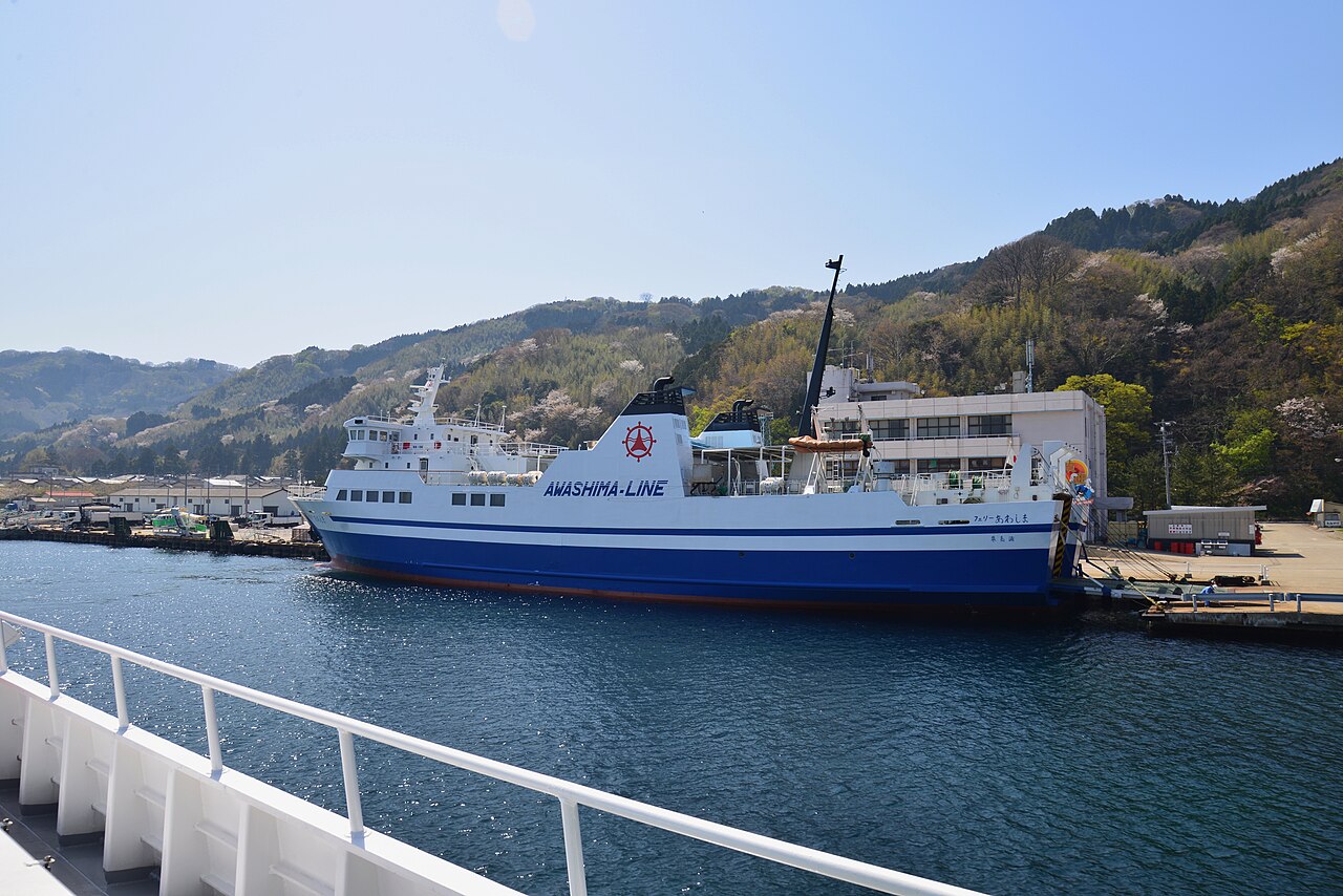 Ferry New Awashima tied up at the port, with cherry blossoms on the hill behind.