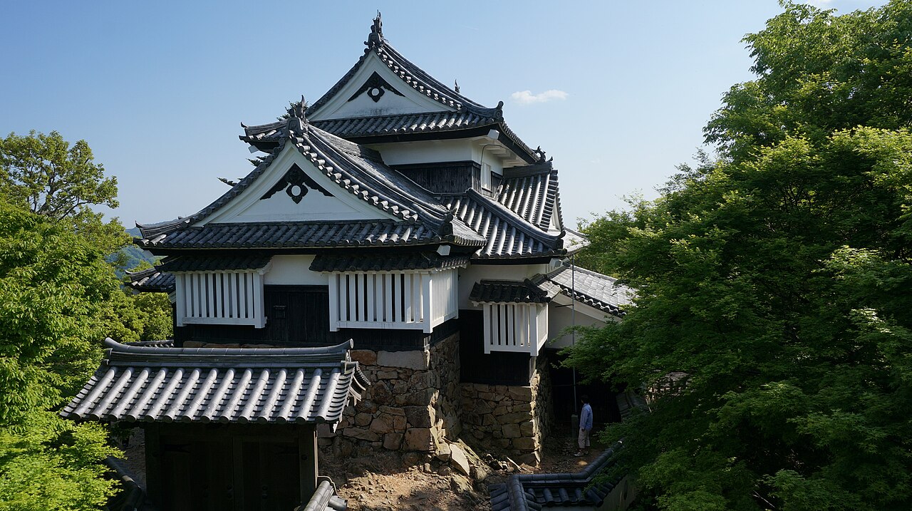 The two-storied keep of Bitchu Matsuyama Castle, with white plaster walls and black-lacquered boards, rising from its stone base among fresh green trees