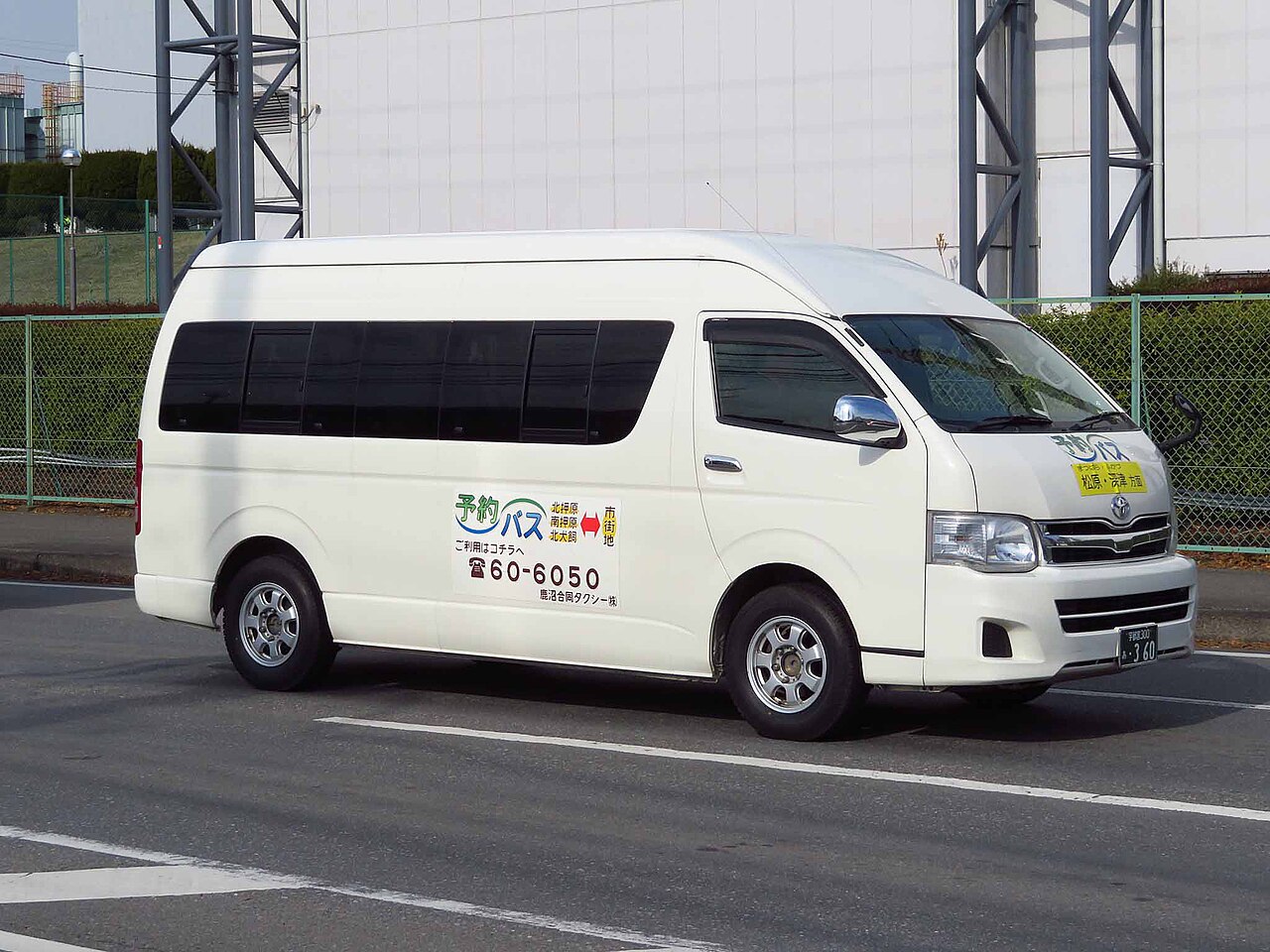 A white minibus van used for a reservation-only local bus service, with its route and booking phone number painted on the side