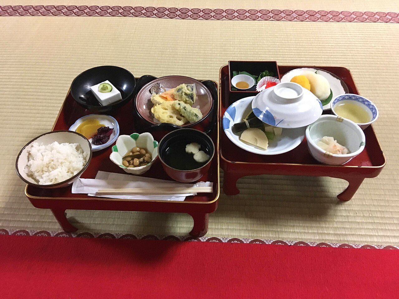 A vegetarian temple lodging dinner on two red lacquered trays set on tatami, with rice, tofu, tempura, soup, pickles and fruit