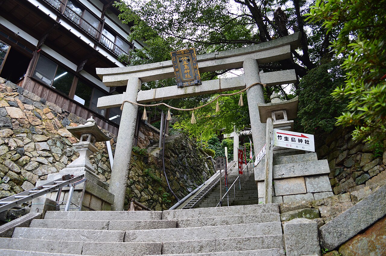 Stone torii with a Tsukubusuma Shrine nameplate at the top of stone steps, with stone lanterns and a mossy retaining wall