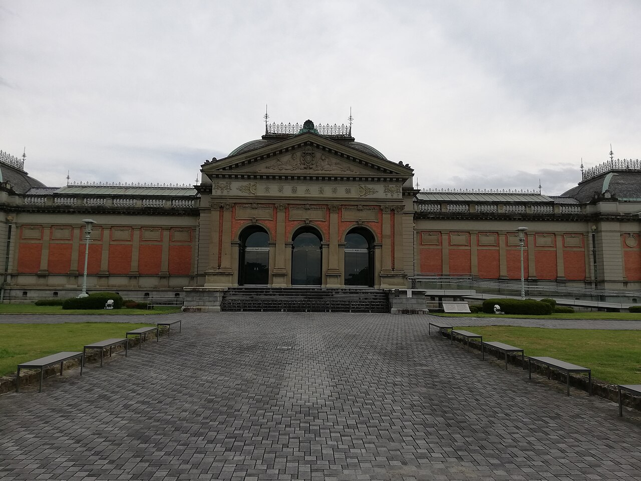 The red-brick main hall of the Kyoto National Museum with a three-arched entrance, seen across a paved forecourt