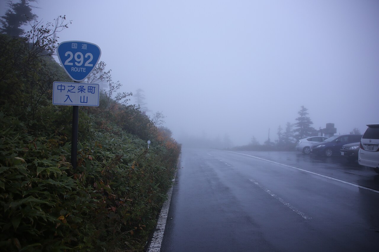 A national route sign beside a misty mountain road and roadside parking at Shibu Pass