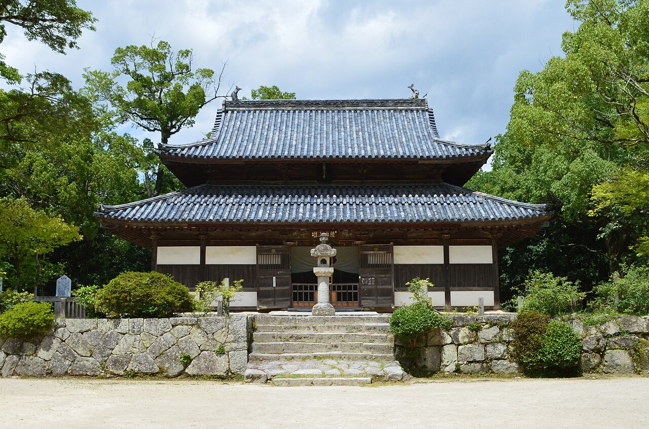 The main hall of Kanzeonji temple and a stone lantern among trees.