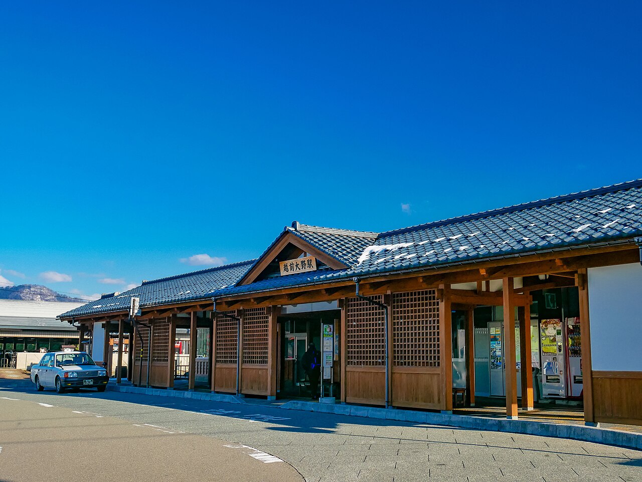 Echizen-Ono Station, a low wooden building with a dark tiled roof and latticed windows under a deep blue sky.