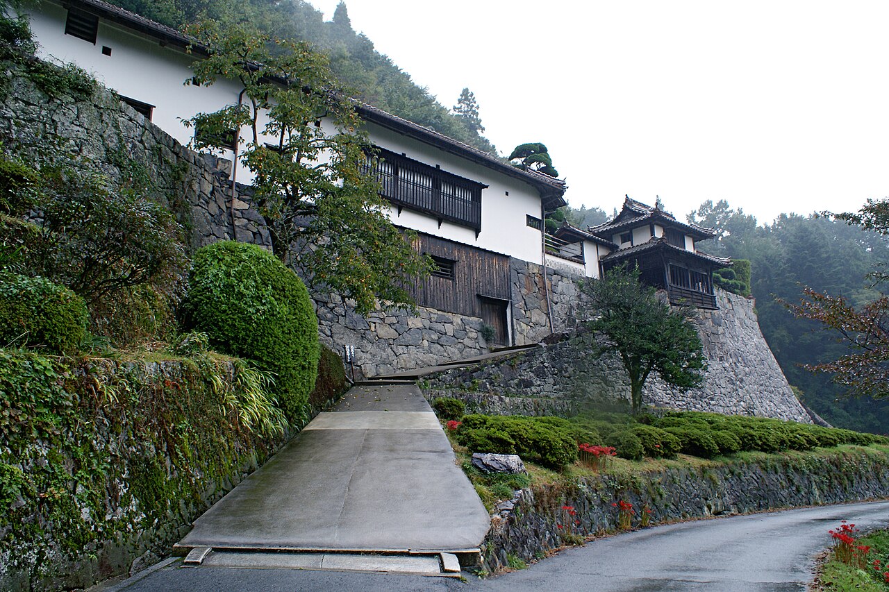 The Hirokane residence on its tall dry-stone foundation, white-walled storehouses and a small tiered turret above a quiet mountain road