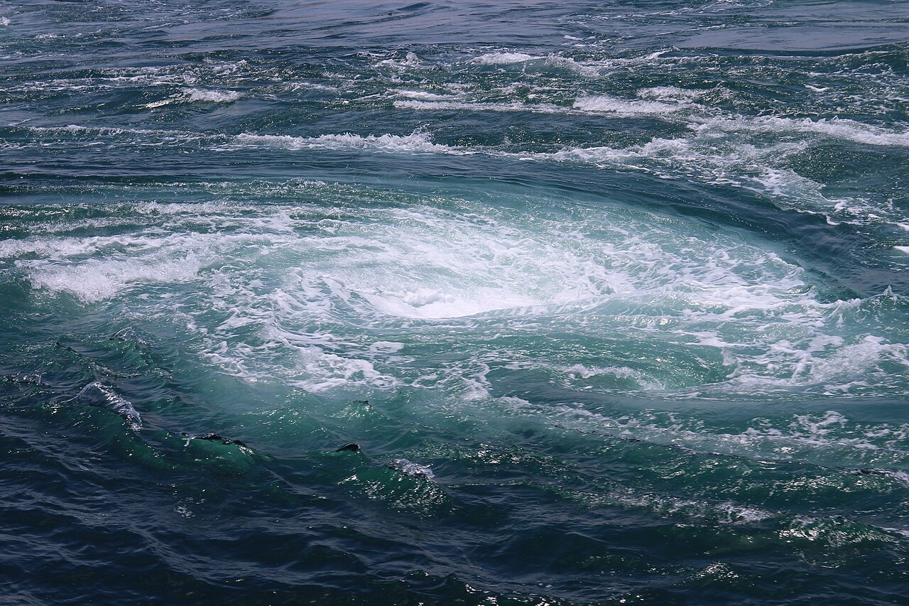 A whirlpool of white foam turning in green water in the Naruto Strait