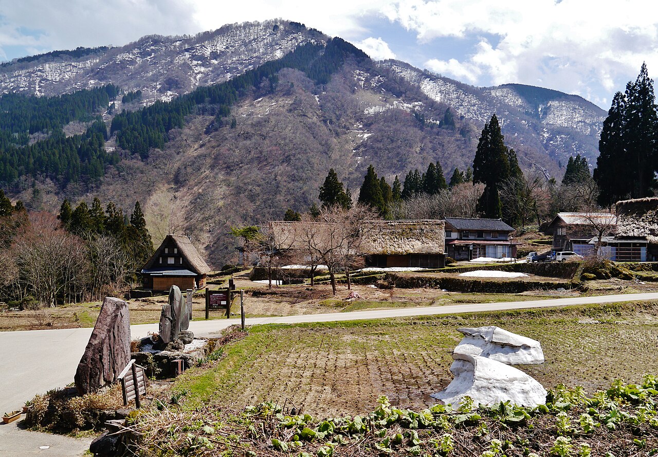 Ainokura gassho-zukuri village with snow-patched mountains rising behind the thatched roofs