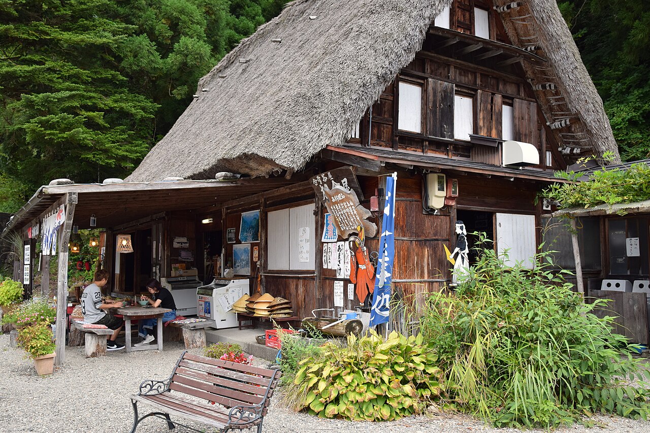 Visitors eating at tables under the eaves of a thatched gassho-zukuri house in Gokayama