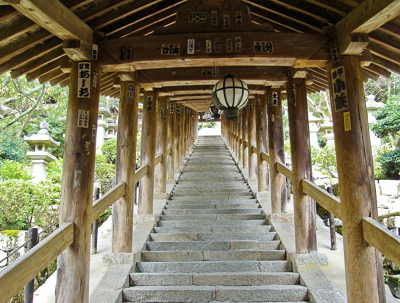 A long covered wooden stairway with hanging lanterns climbing the slope at Hasedera temple