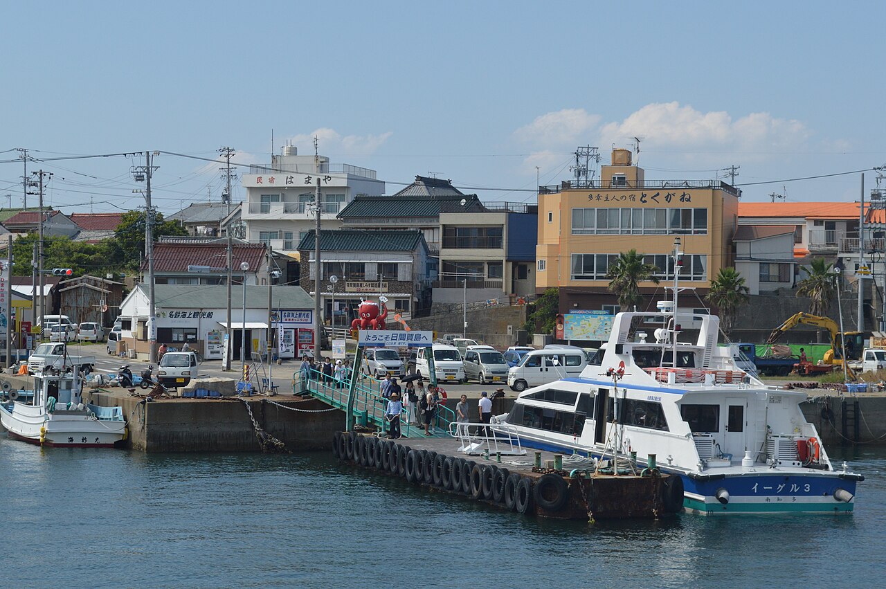 Passengers walking up the pier at Himakajima West Port past a welcome sign and a red octopus statue, with a high-speed boat alongside.