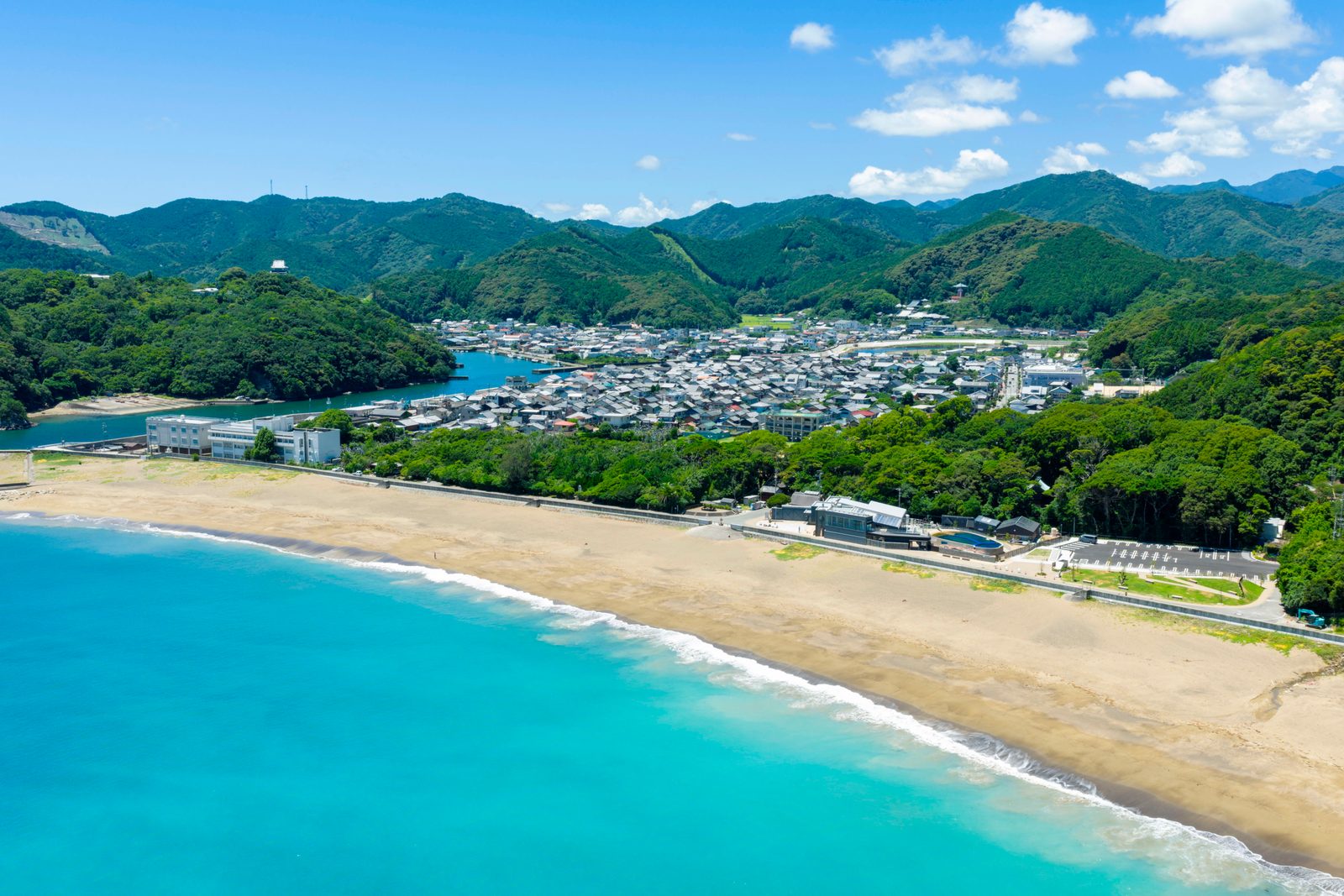 Ohama Beach curving below green hills with the rooftops of Hiwasa behind it, seen from above
