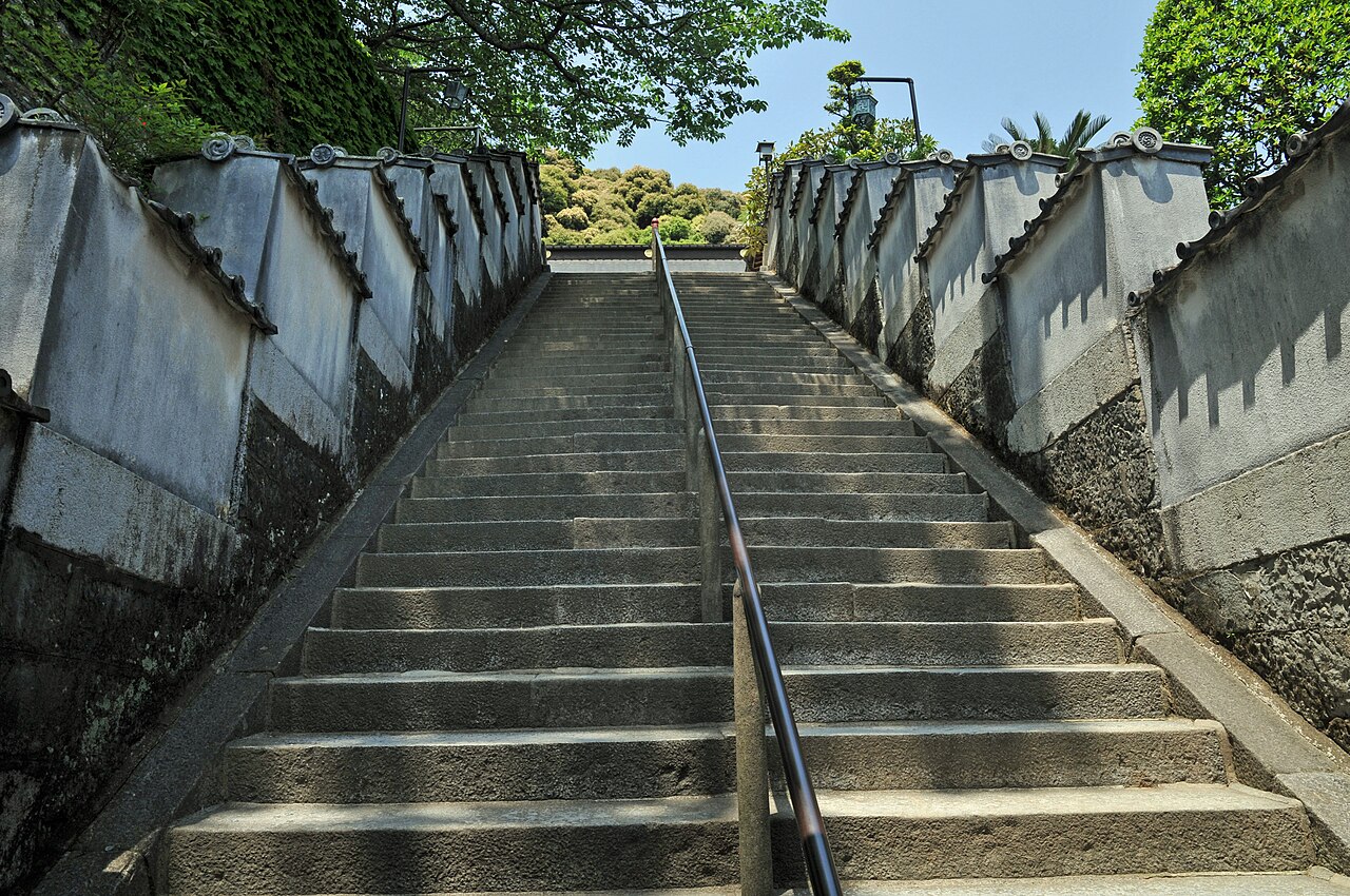 A long stone stairway between white plaster walls climbing to Yakuoji